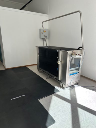 Große, silberne Maschine mit Kontrollpaneel, in einem hellen, leeren Raum.